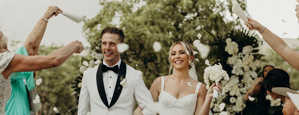 Bride and groom smiling as they exit the wedding ceremony with their guests tossing white rose petals during their classy Nizuc Resort and Spa Wedding