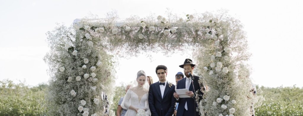 Bride and groom standing underneath wedding arch with officiant during their dreamy wedding ceremony in Cancun at the Nizuc Resort and Spa
